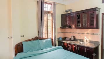 A bedroom with a bed, a window with curtains, a kitchen area with cabinets and a sink.