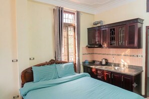 Ein Schlafzimmer mit einem Bett, einem Fenster mit Vorhängen, einer Küchenzeile mit Schränken und einer Spüle.