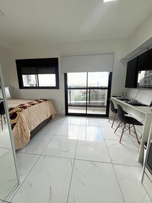 Quarto de hotel moderno com cama, escrivaninha e uma janela ampla.