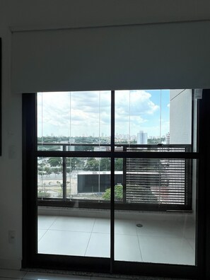 A room with a large window offering a view of a cityscape and a parking lot. - Refúgio do Brooklin 230m do metrô (São Paulo)