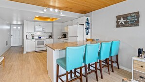 A modern kitchen with white cabinets, a central island with bar stools, and a wooden ceiling. - Beachfront 4th Floor Condo with Spectacular Beach & Ocean Views and Pool! (New Smyrna Beach)