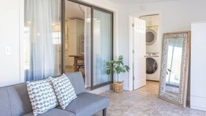 A modern living room with a grey sofa, a large sliding glass door leading to a laundry area, and a potted plant. - Panama City Beach -Beach House | Walk to Beach | Backyard Hangout | Sleeps 8 (Panama City Beach)