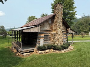 A rustic log cabin with a stone chimney, a porch, and a small window. - Mountian “Silo-tude” (Sevierville)