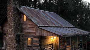 A rustic log cabin with a stone chimney, a porch with a wagon wheel, and a welcoming light. - Mountian “Silo-tude” (Sevierville)