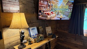 A cozy cabin interior with a wooden wall, a television displaying a cabin scene, a lamp, a remote control, and a welcome sign. - Mountian “Silo-tude” (Sevierville)
