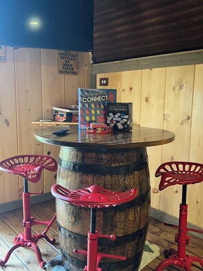 A wooden barrel table with a Connect4 game box and a Double-Fifteen Dominoes box on top. - Mountian “Silo-tude” (Sevierville)