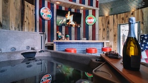 A bar area with a wooden backdrop, a television displaying a fire, and a bottle of wine on the counter. - Mountian “Silo-tude” (Sevierville)