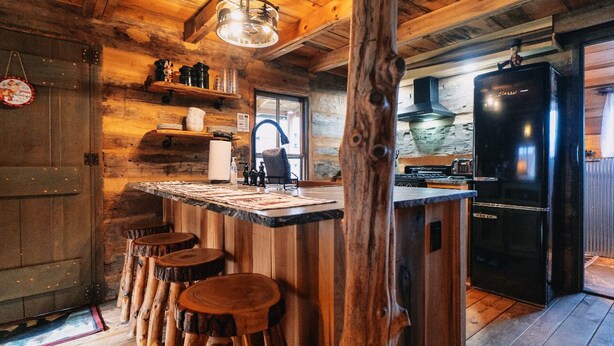 A rustic kitchen with wooden walls, a central island with stools, a black refrigerator, and a hanging light fixture. - Mountian “Silo-tude” (Sevierville)