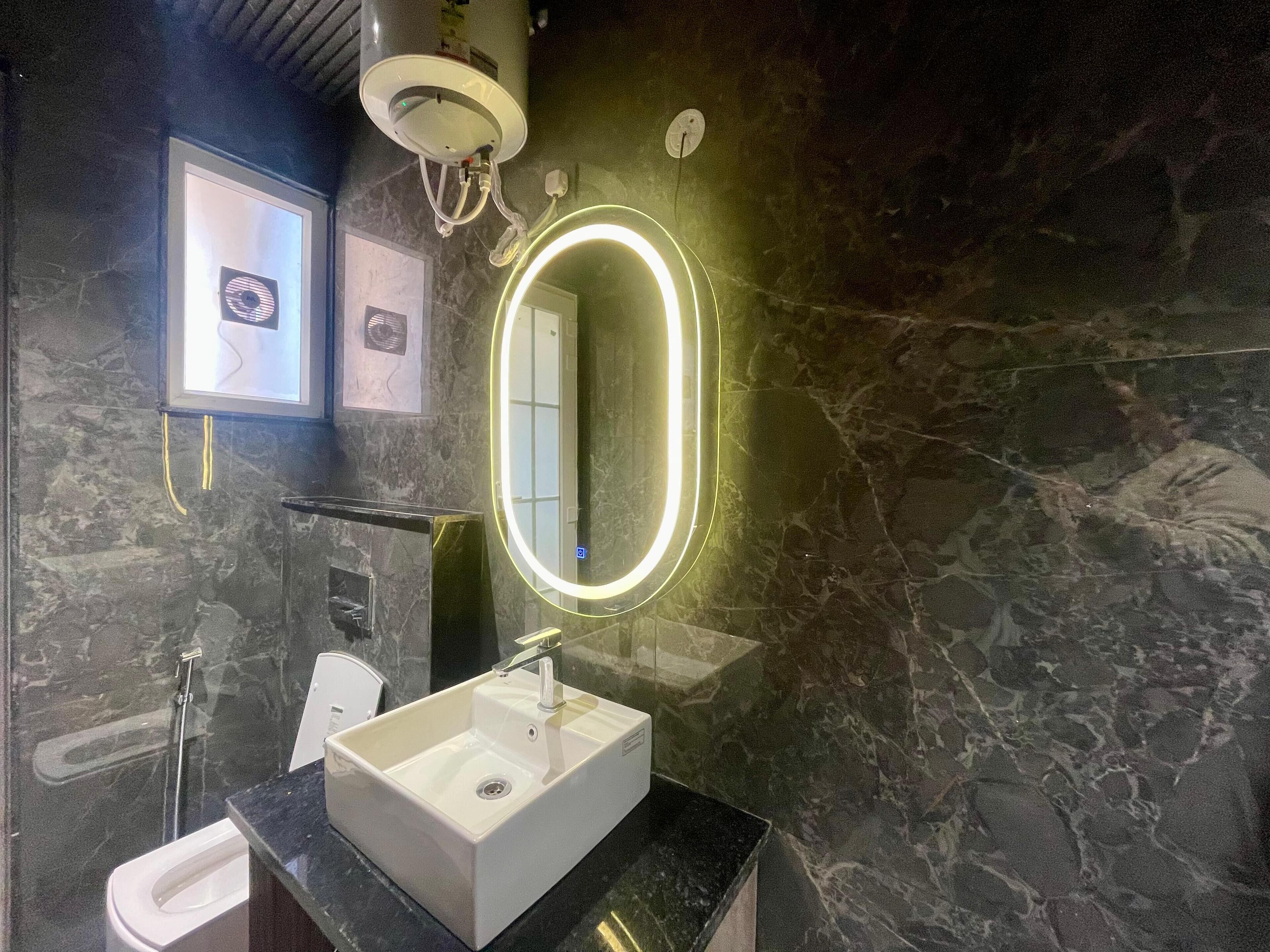 A bathroom with a white sink, a mirror with a neon light, a shower, and a marble wall.