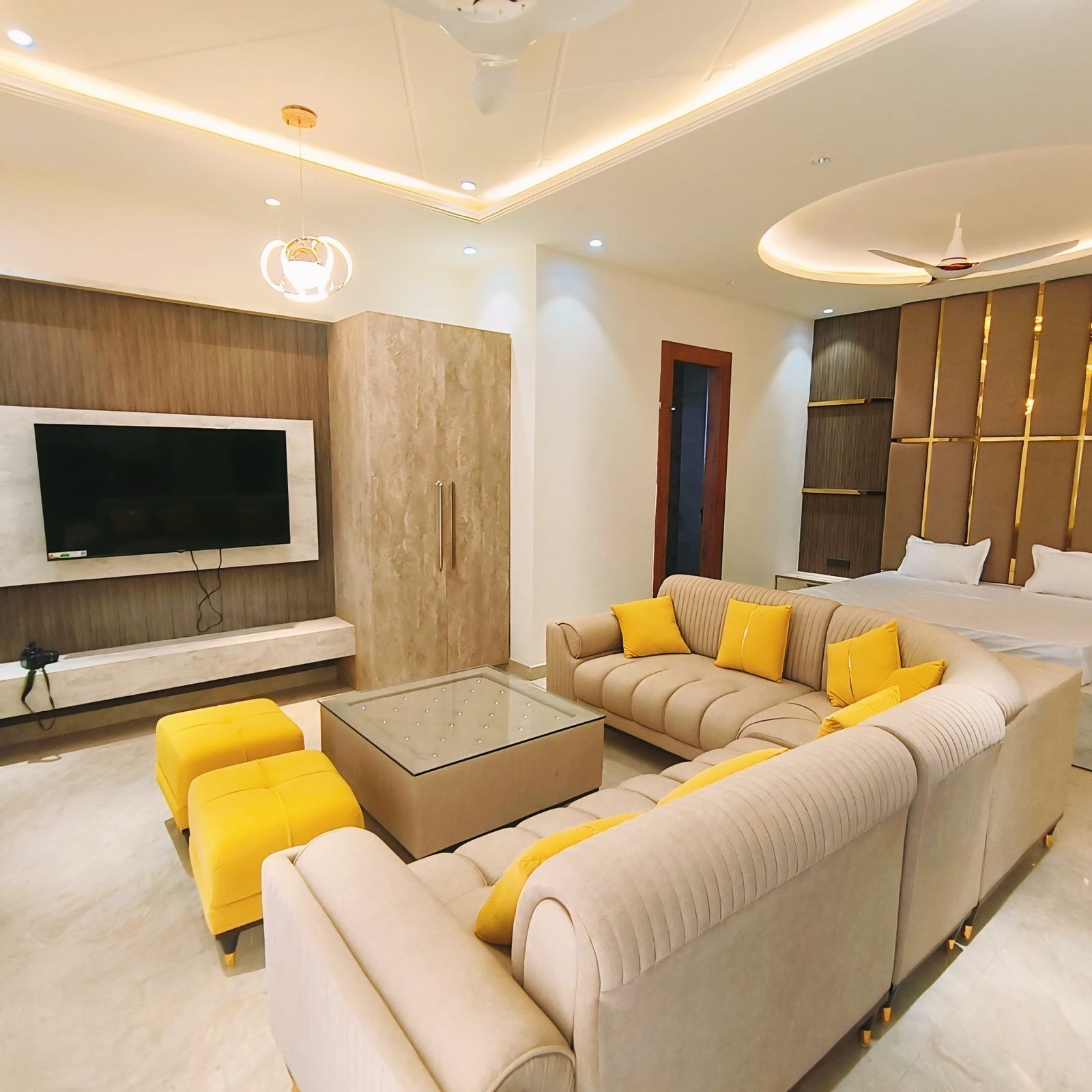 A modern living room with a sectional sofa, a glass coffee table, and a flat-screen TV mounted on the wall.