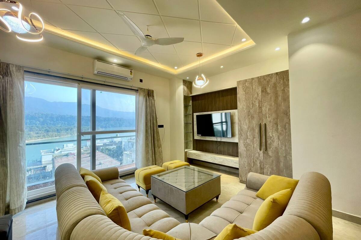 Una sala de estar moderna con un conjunto de sofá, una mesa de centro de vidrio y un televisor instalado en un panel de madera.