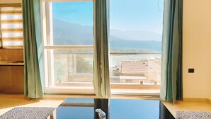 Una stanza con un'ampia finestra, un tavolo nero, cuscini decorati e vista su montagne e palazzi.