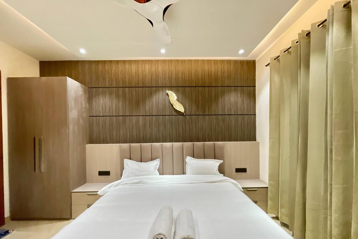 Una habitación de hotel moderna con una cama grande, un panel de pared de madera y un ventanal con cortinas.
