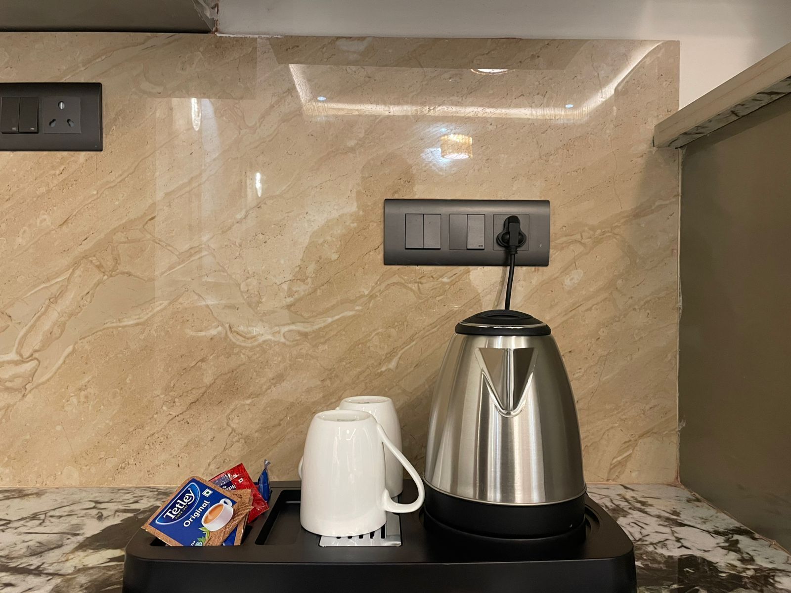 A coffee station with a coffee maker, two white cups, and a tray with coffee packets.
