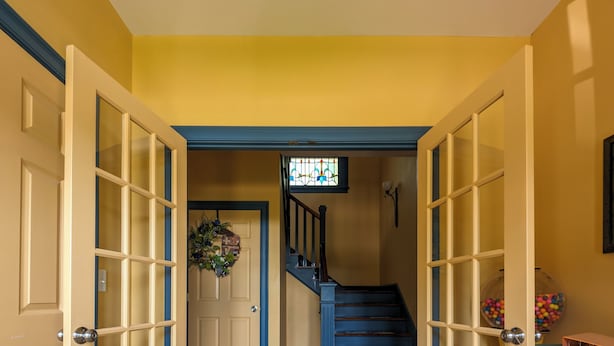 Un pasillo con una escalera de madera, una puerta con paneles de vidrio y una lámpara fijada a la pared.
