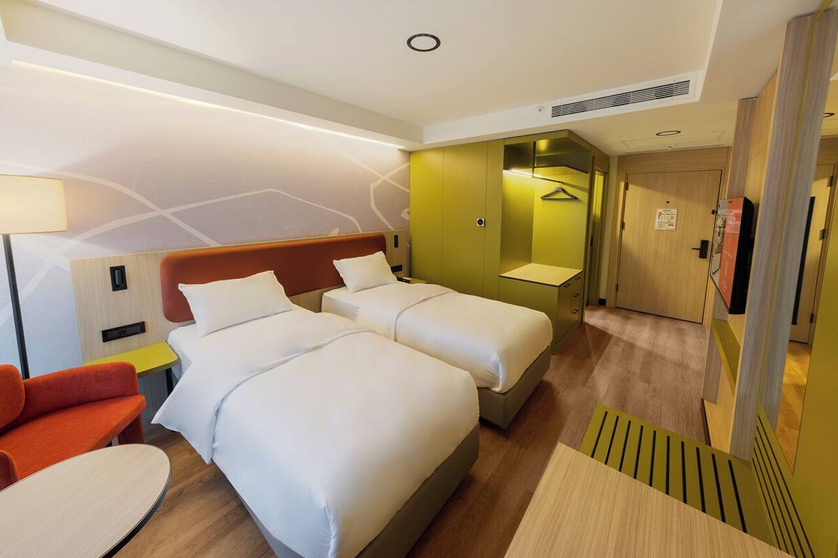 A hotel room with two beds, a sofa, a desk, and a bathroom.