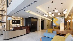 Un moderno vestíbulo de hotel con una recepción, una zona de estar con sofás y una mesa de ajedrez.