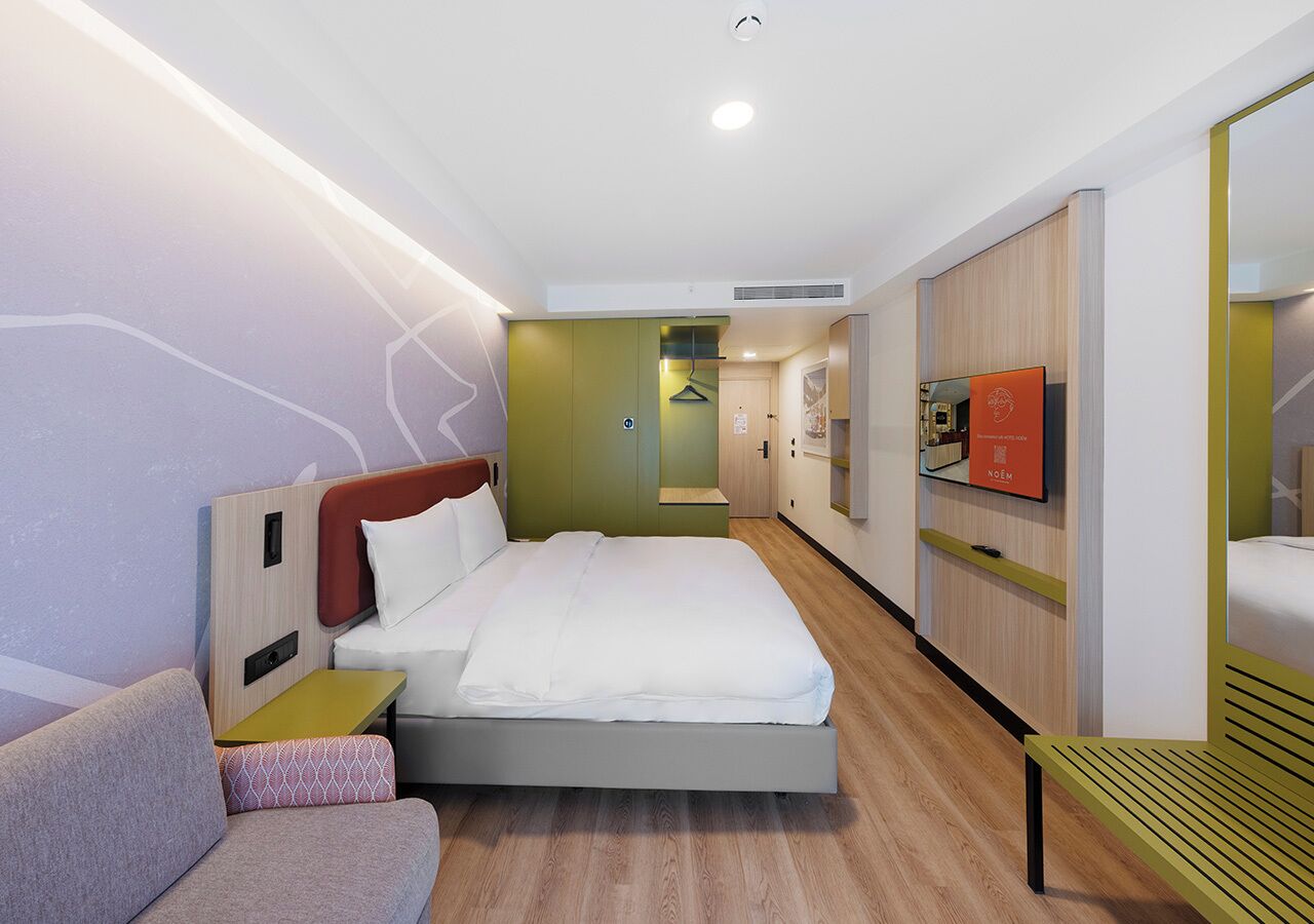 Ein modernes Hotelzimmer mit einem Bett, einer Couch, einem Fernseher und einem kleinen Tisch.
