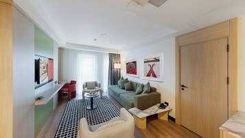 Una camera d'albergo moderna con divano, un tavolino, una sedia, televisore e armadio.