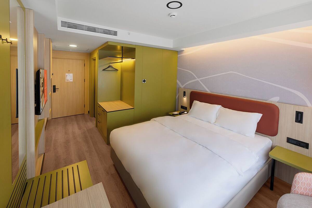 A hotel room with a large bed, a bedside table, a nightstand, a wardrobe, a mirror, and a door.
