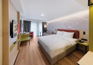 Una habitación de hotel moderna con una cama grande, un escritorio, una silla y un televisor montado en la pared.