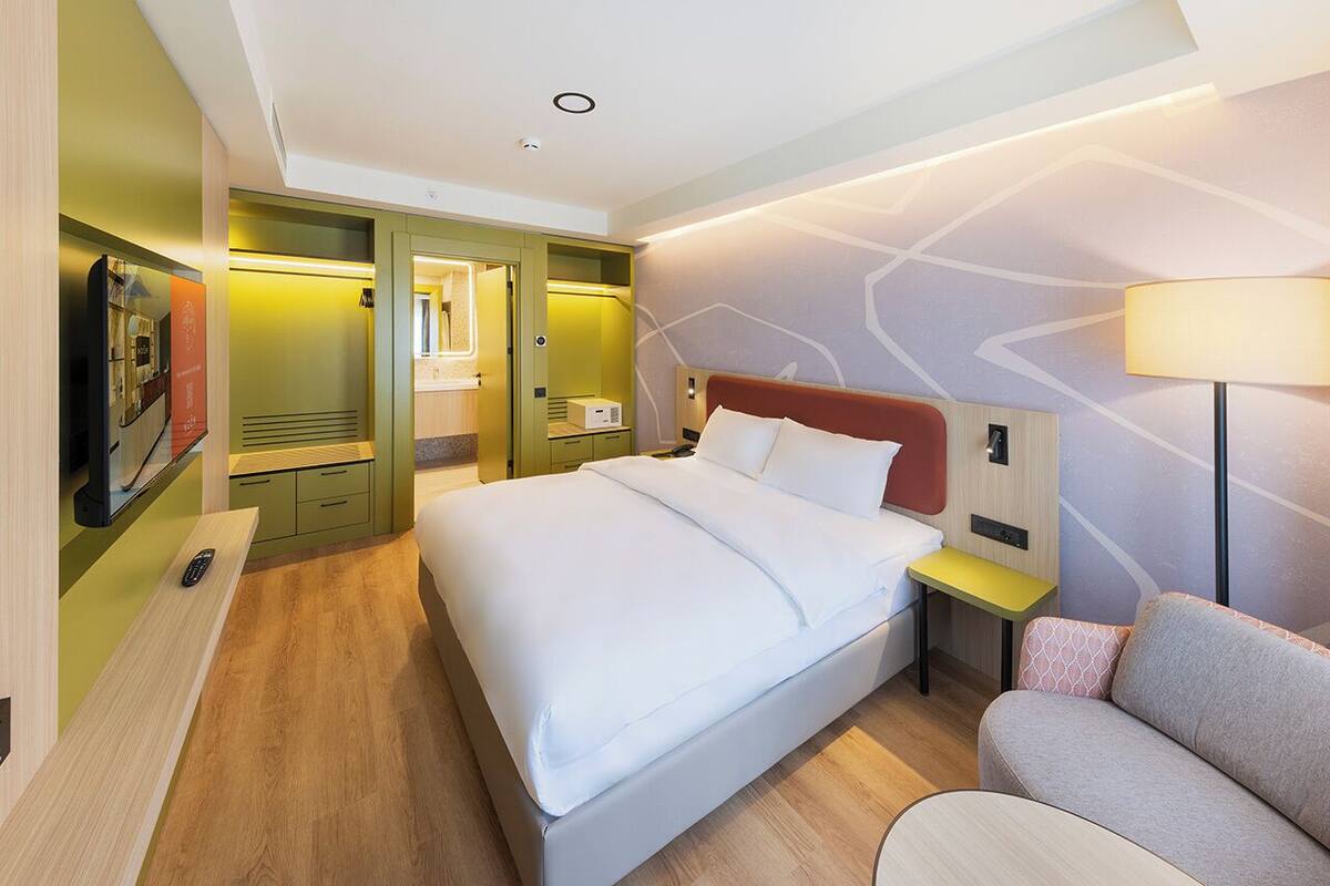 A modern hotel room with a large bed, bedside tables, a sofa, and a TV.