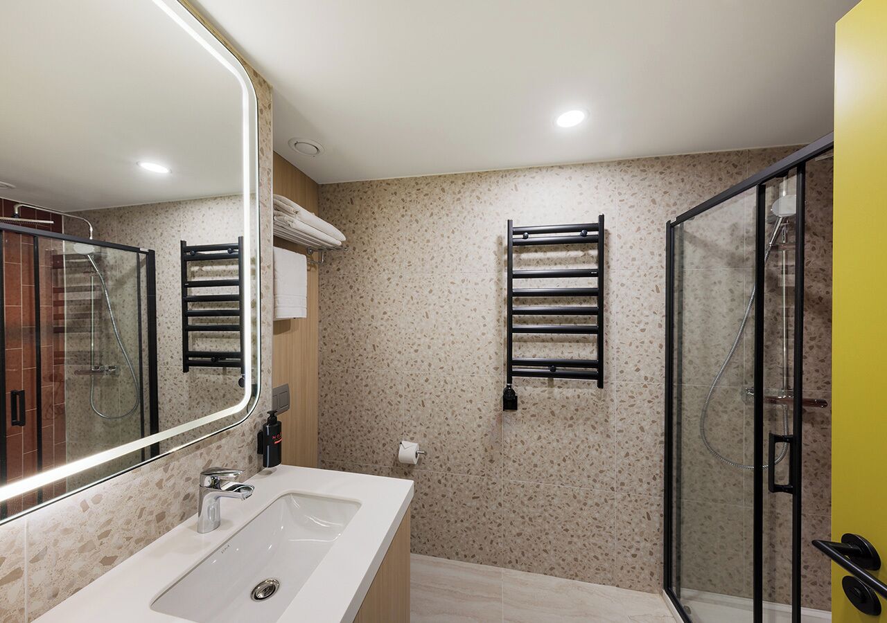 A modern bathroom with a large mirror, a sink, a glass shower enclosure, and two towel racks on the wall.