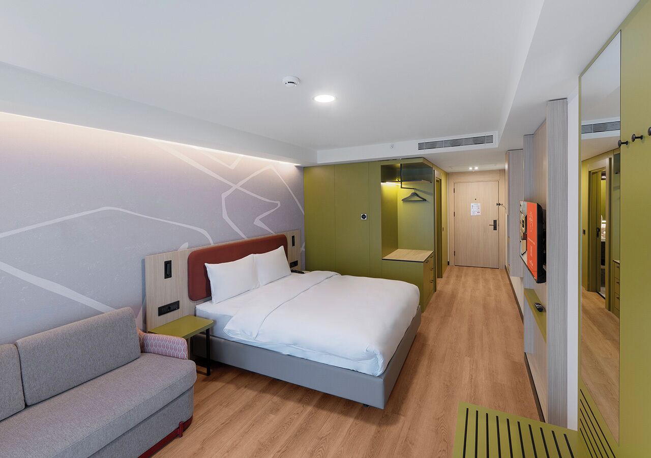 A modern hotel room with a bed, a sofa, a bedside table, and a TV.