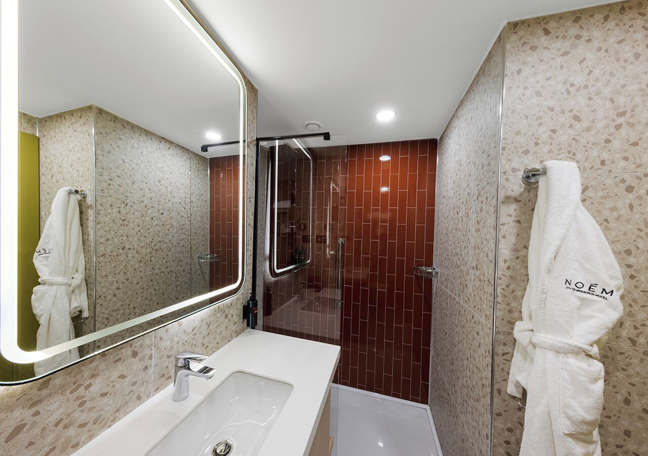 A modern bathroom with a large mirror, a sink, a shower area, and a robe hanging on the wall.