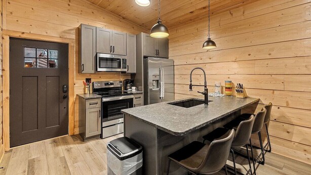 Una cocina moderna con paredes de madera, electrodomésticos de acero inoxidable y una isla central con taburetes de bar.