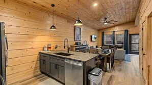 Una cocina moderna con paredes de madera, una isla central, electrodomésticos de acero inoxidable, iluminación colgante y un ventilador de techo.