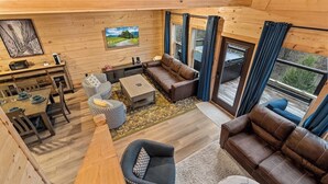 Interior acogedor de una cabaña con comedor, sofá, mesa de centro y un gran ventanal con cortinas.