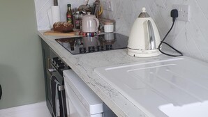 A kitchen with a white countertop, a stove, a kettle, and various kitchen items. - Apartment-sleeps2-parking-garden-patio (Castleisland)