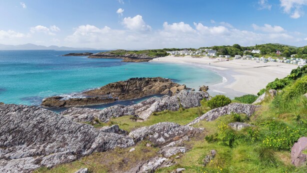 A coastal landscape with a sandy beach, rocky outcrops, and a row of houses along the shore. - Apartment-sleeps2-parking-garden-patio (Castleisland)