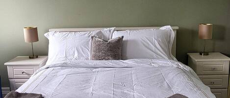 A neatly made bed with white linens, two bedside tables with lamps, and a green wall.