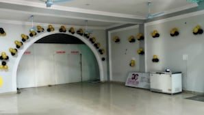 A spacious room with a high ceiling, white walls, and a tiled floor. There are ceiling fans, a refrigerator, and a sign indicating a changing room. - Hotel Datia Comfort Inn (Datia)