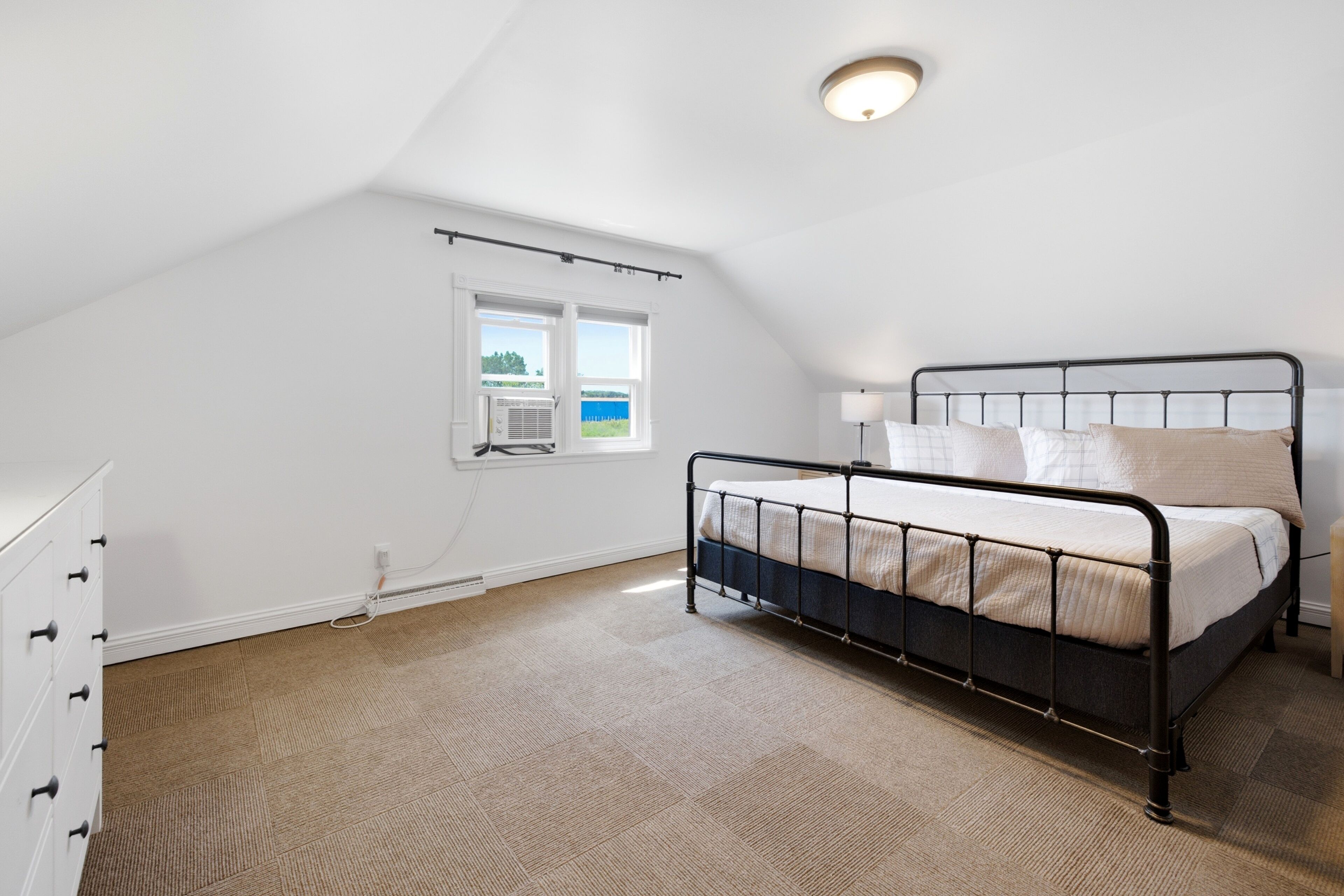 Un dormitorio con cama, cómoda, ventana y lámpara en el techo.