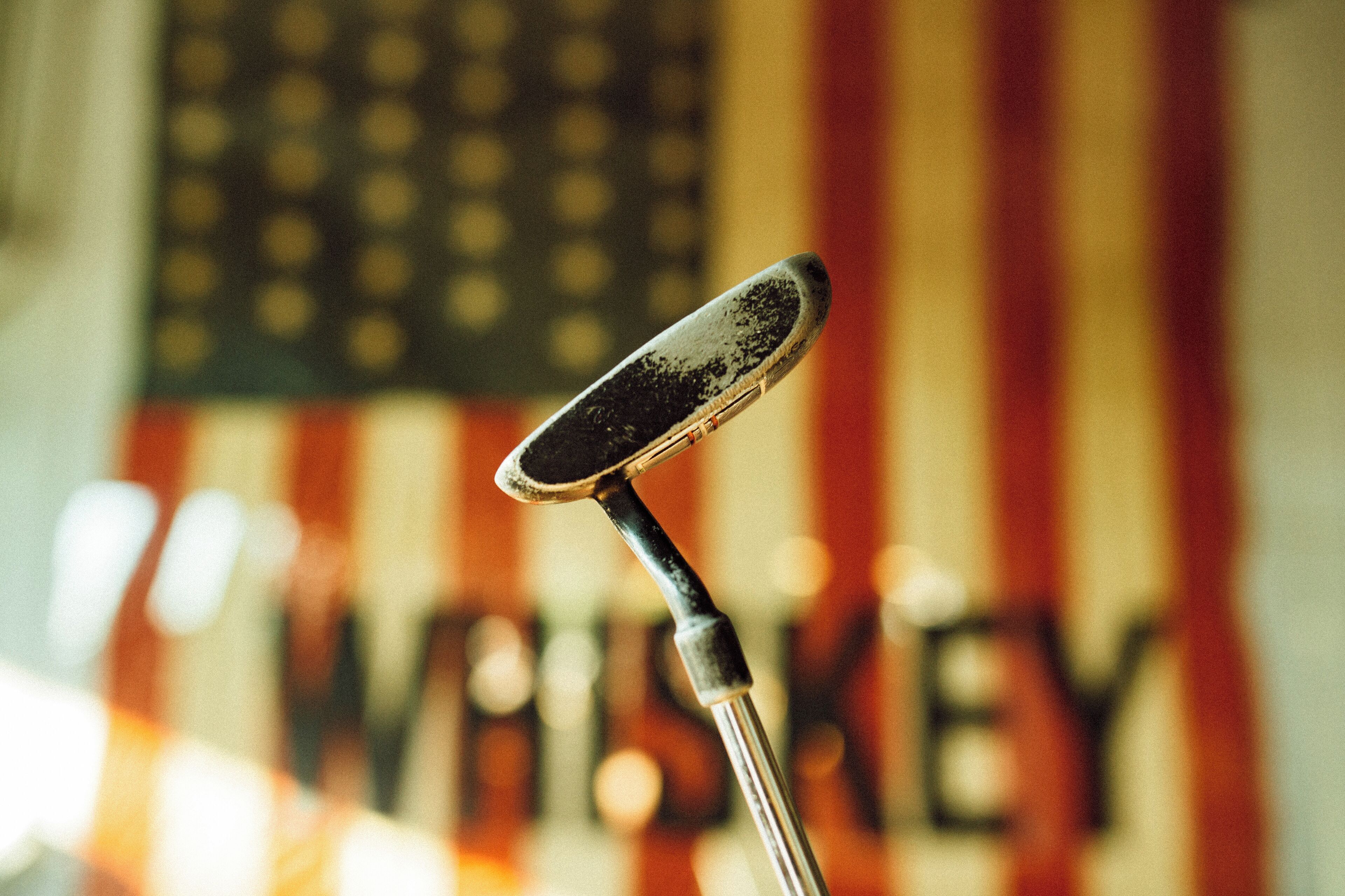 A microphone with a blurred American flag and the word "WHISKEY" in the background.