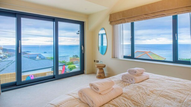 Une chambre avec un grand lit, une vue sur la mer et un balcon où est posée une planche de surf.
