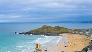 Une plage côtière avec un fort historique situé sur une colline, une plage de sable et une mer calme.