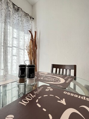 Enjoy meals in this dining area with a glass table, brown placemat, and a vase with dried reeds.