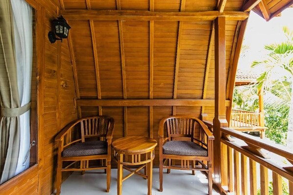 Ein Holzbalkon mit zwei Holzsesseln und einem kleinen Tisch, mit Blick auf einen üppigen Garten.