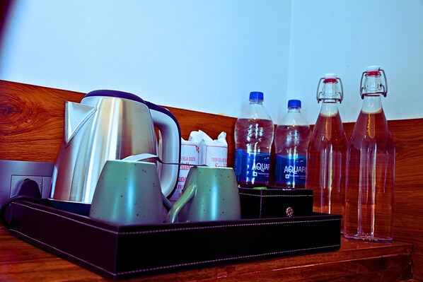 Minibar de una habitación de hotel con cafetera, hervidor de agua y botellas de agua y zumo.