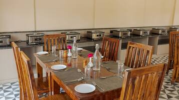 Un coin repas avec une longue table en bois, dressée pour six personnes, agrémentée de grille-pains, de salières et de poivrières, et d’un vase contenant une fleur rose.