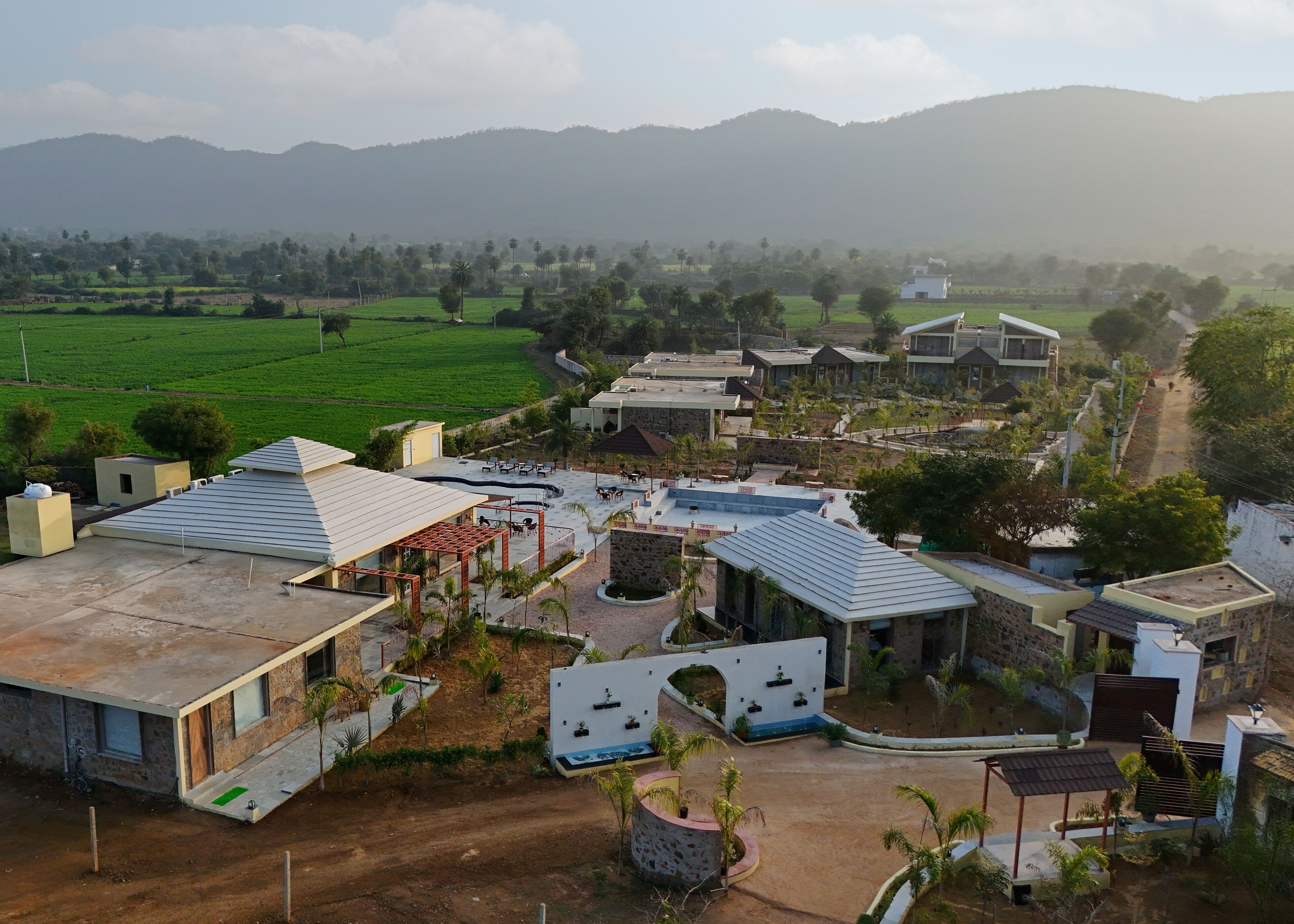 A residential area with houses, a paved road, and green fields in the background.