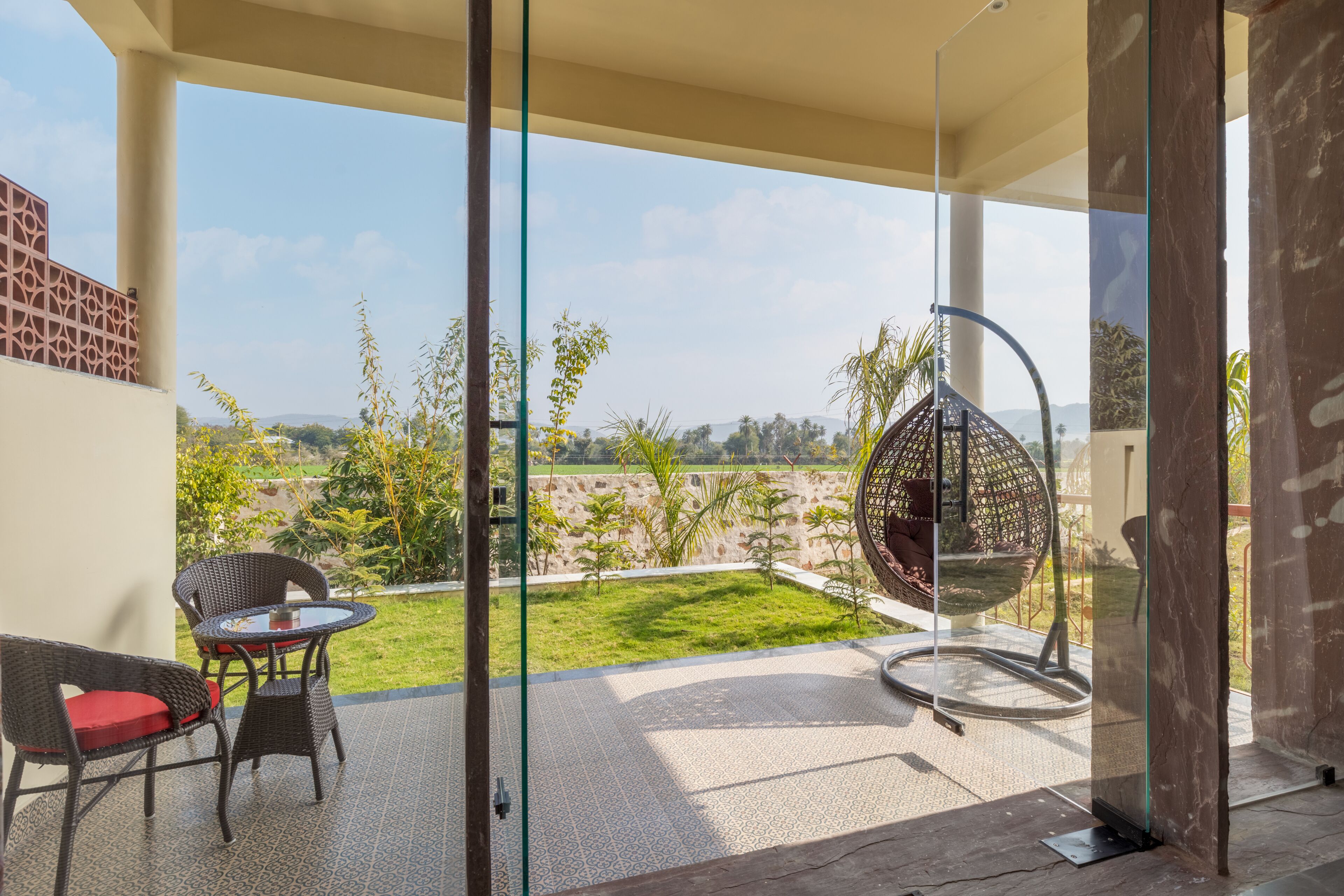 A modern patio with a glass door, a round table, wicker chairs, and a hanging chair.