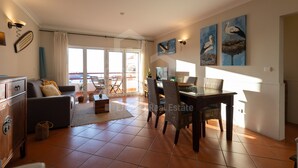 Un vaste espace de vie comprenant un canapé, une table à manger et des chaises, un balcon avec vue et des œuvres d’art accrochées aux murs.