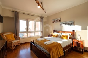 A bedroom with a bed, a chair, a nightstand, a lamp, and a window.