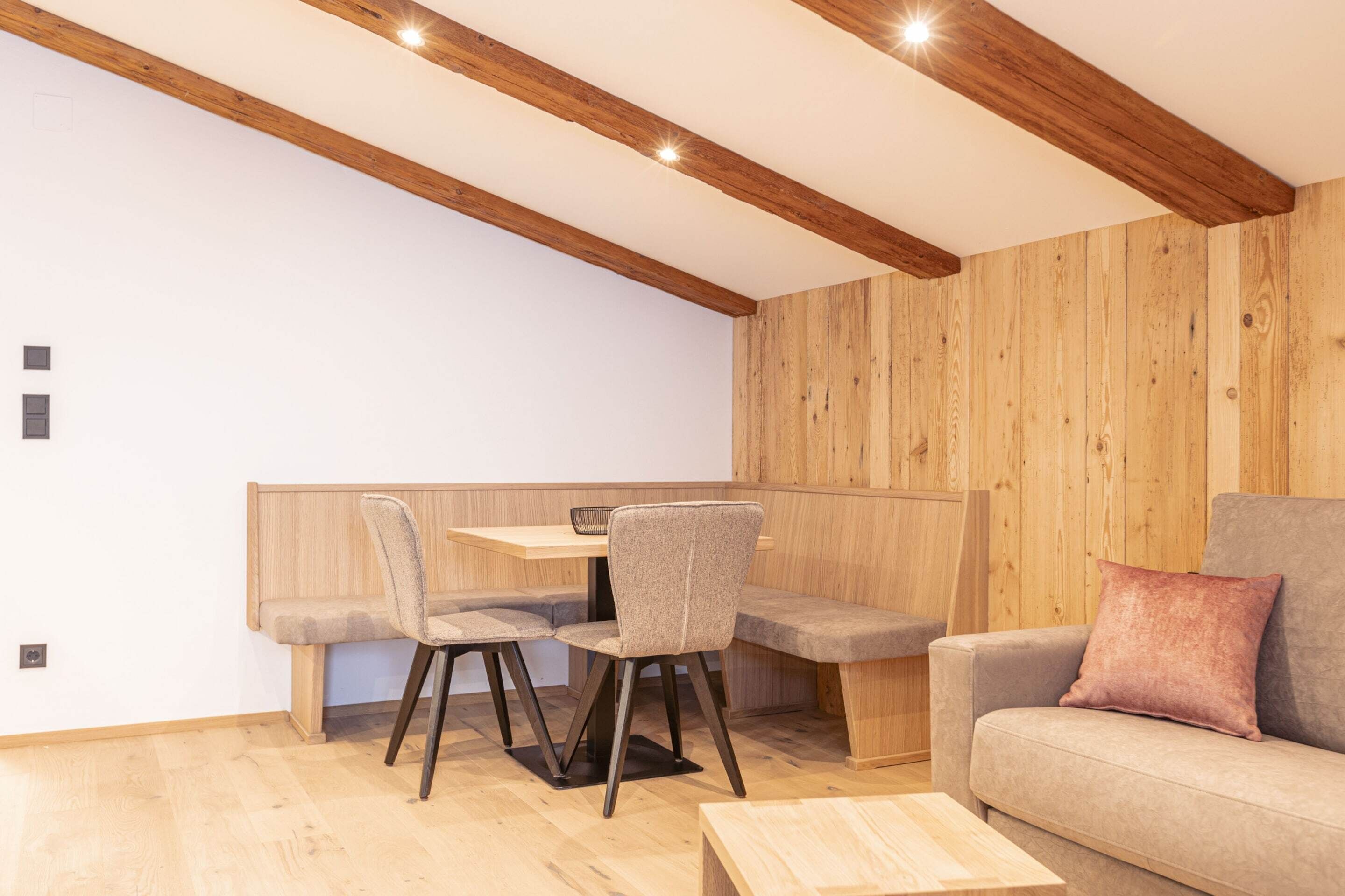 A modern living room with a wooden ceiling, a sofa, a coffee table, and a dining area with chairs and a table.