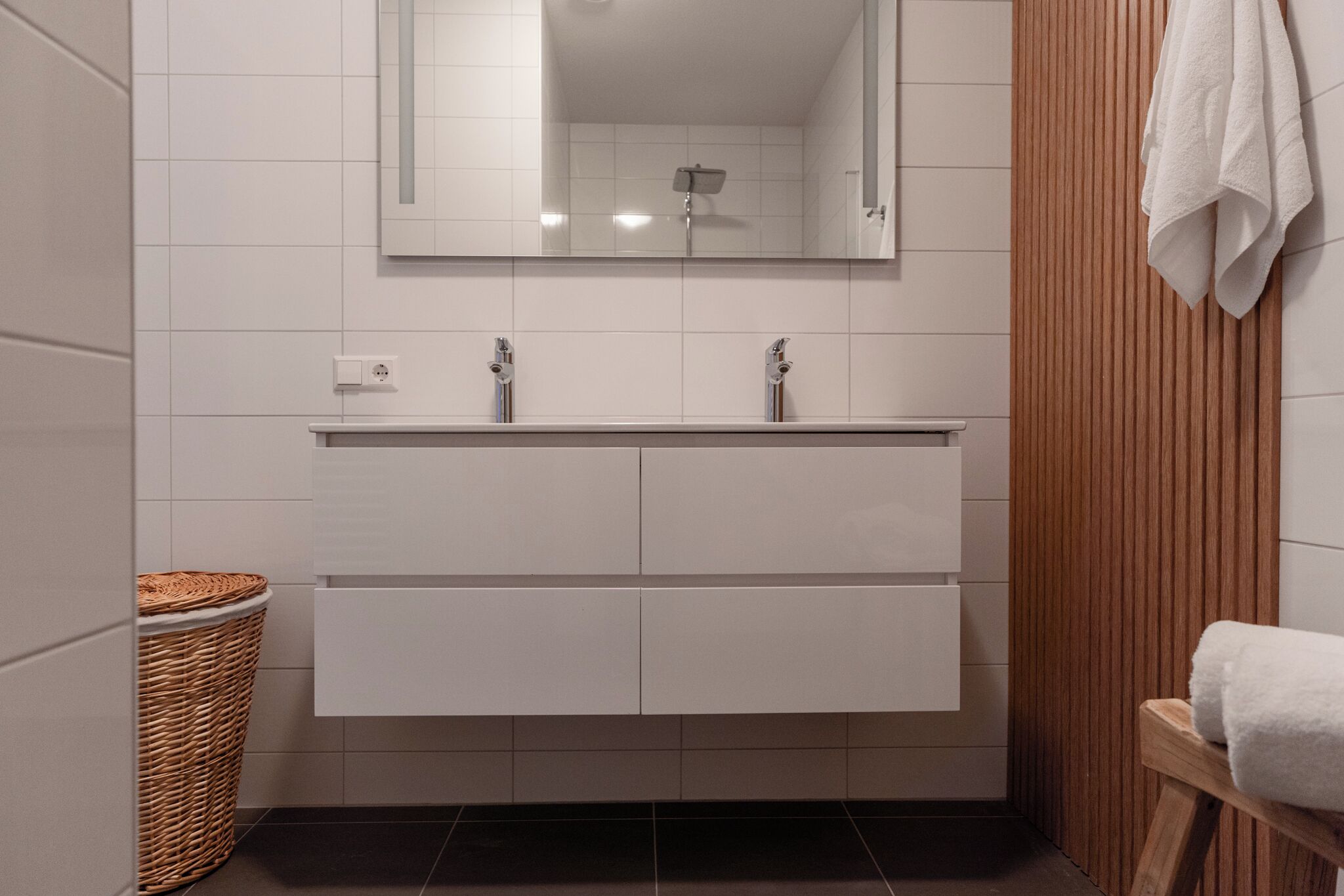A bathroom with a white vanity, a mirror, a shower, and a wooden panel on the wall.
